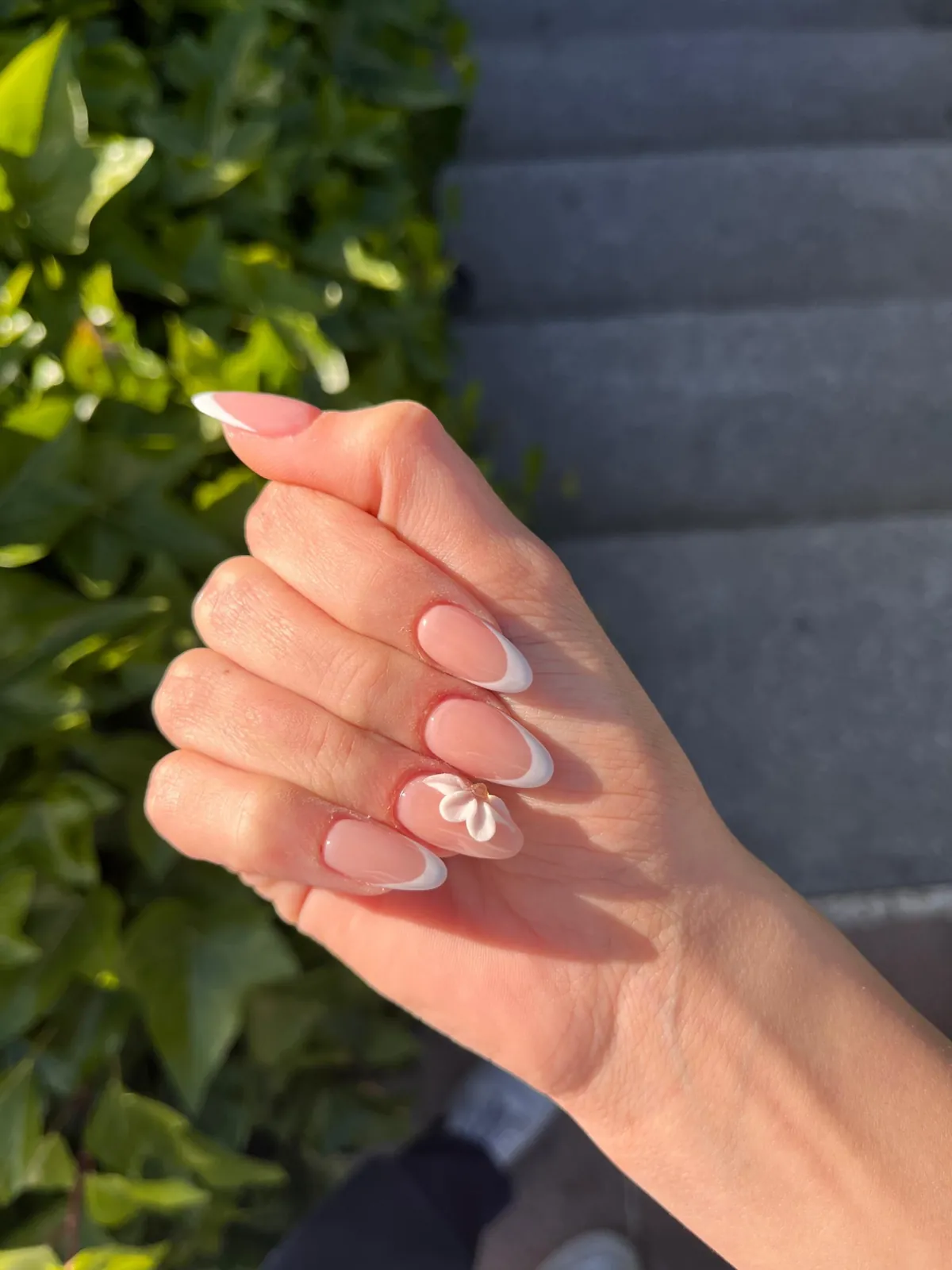Manicura francesa con flor en relieve a la luz del sol