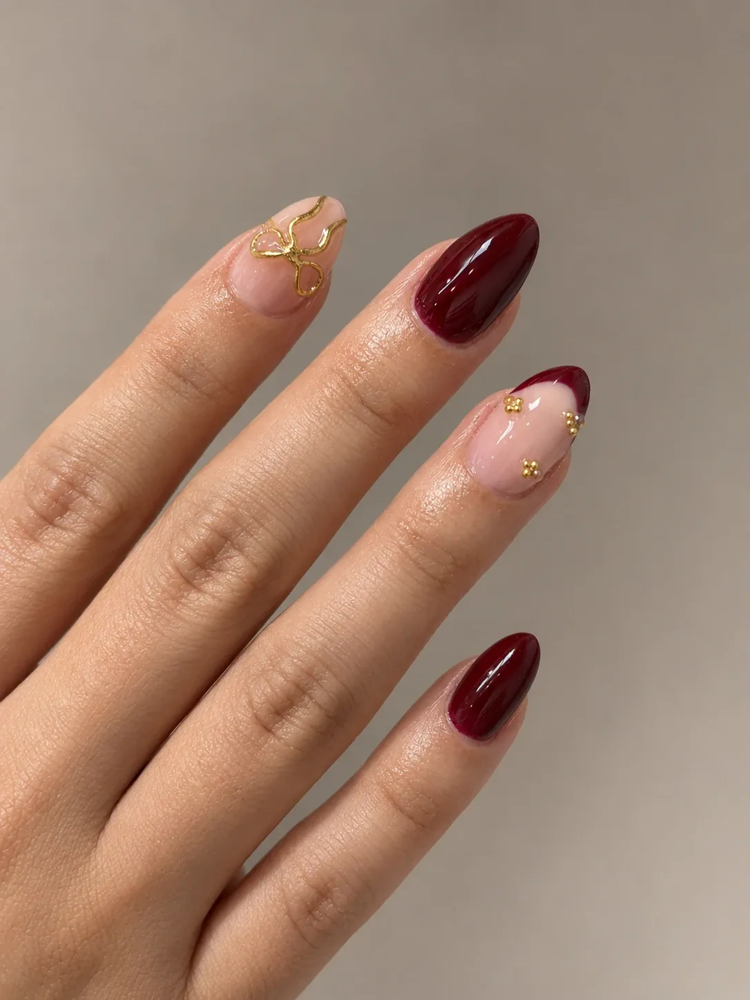 Manicura en tono burdeos con lazo dorado pintado a mano